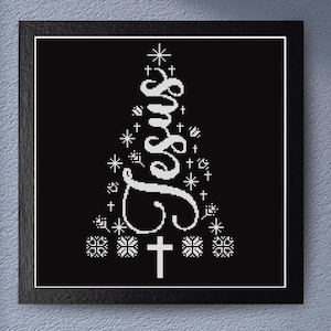 Könnte beinhalten: Schwarz gerahmtes Kunstwerk mit einem weißen Kreuzstich-Design. Das Design zeigt das Wort "Jesus" in einer stilisierten Schriftart, angeordnet in Form eines Weihnachtsbaums, mit Kreuzen und Schneeflocken-Akzenten. Das Kunstwerk wird vor einer grauen Wand ausgestellt.