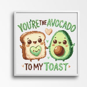 Puede incluir: Un bordado de punto de cruz enmarcado con una linda pareja de aguacate y tostada tomados de la mano. El aguacate tiene un hueso marrón y la tostada un corazón verde. El texto dice: "You're the avocado to my toast."