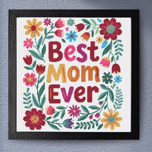 Może przedstawiać: Oprawiony wzór haftu krzyżykowego ze słowami "Best Mom Ever" w kolorowych literach. Tekst otoczony jest żywą kwiatową obwódką z czerwonymi, różowymi, żółtymi i niebieskimi kwiatami z zielonymi liśćmi. Rama jest czarna.