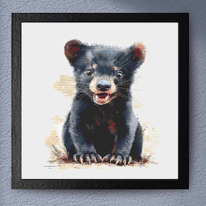 May include: A black bear cub with a white patch on its chest sits on a brown background. The cub has a wide, toothy grin and its eyes are open wide.