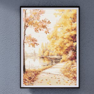 Op de afbeelding: Ingelijste kunstafdruk met een herfstlandschap. Het kunstwerk toont een pad dat door een park loopt met bomen in herfstkleuren geel, oranje en bruin. Een meer weerspiegelt de bomen en de lucht. De afdruk zit in een zwarte lijst.