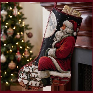 Op de afbeelding: Een zwarte kerstkous met een geweven tapijtdesign van de Kerstman zittend op een bakstenen schoorsteen onder een volle maan. De scène bevat een besneeuwd dorp aan de onderkant, met een cadeau dat uit de opening aan de bovenkant steekt.
