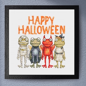 May include: A framed print featuring four cartoon frogs dressed in Halloween costumes. The frogs are dressed as a mummy, a vampire, a devil, and a witch. The words "HAPPY HALLOWEEN" are written in orange above the frogs.