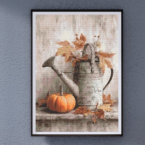 Puede incluir: Impresión enmarcada que presenta una naturaleza muerta. Una calabaza naranja se encuentra junto a una regadera de metal desgastado, adornada con hojas de otoño. El fondo tiene un aspecto texturizado y rústico, evocando un tema de cosecha.