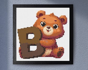 May include: A framed cross-stitch design featuring a brown teddy bear holding a brown letter "B". The bear has a smiling face and is set against a white background. The artwork is framed in a black square frame.