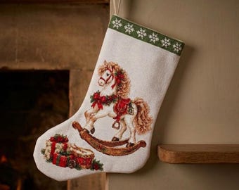 May include: A cream-coloured Christmas stocking featuring a woven design of a brown rocking horse with a red saddle and bridle, adorned with a green wreath. The top border has a green band with white snowflakes, and wrapped gifts sit below.