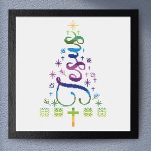 May include: A framed cross-stitch artwork featuring the word "Jesus" in a colorful, stylized tree design. The word is in shades of blue, green, and purple, with crosses and stars. The artwork is framed in a black square frame.