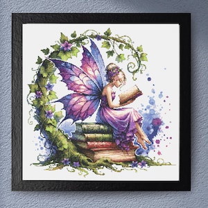 Op de afbeelding: Een ingelijste print toont een fee met paarse en roze vleugels, die een boek leest terwijl ze op een stapel boeken zit. De fee is omgeven door een groene wijnboog met paarse bloemen. Blauwe en paarse aquarelspatten zijn op de achtergrond.