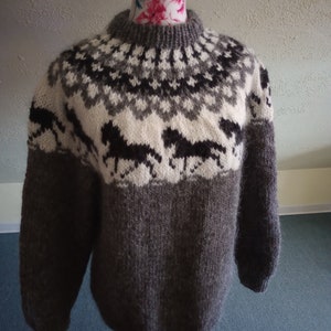 Könnte beinhalten: Ein brauner Wollpullover mit einem weißen und schwarzen geometrischen Muster mit Pferden. Der Pullover hat einen Rundhalsausschnitt und lange Ärmel.