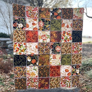May include: A patchwork quilt with a variety of fall-themed fabrics. The quilt is made up of squares of different colors and patterns, including pumpkins, leaves, and flowers. The quilt is a warm and inviting piece of home decor.