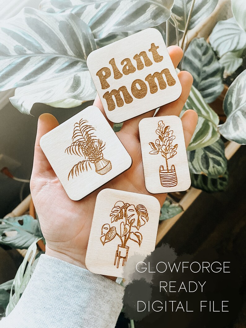 May include: Four wooden plant-themed signs with laser-cut designs. The signs feature a monstera plant, a fern, a flowering plant, and the text "Plant Mom". The signs are ready to be cut on a Glowforge.