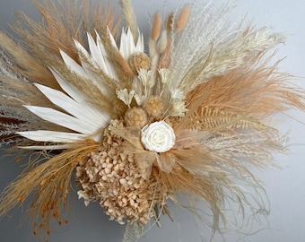 May include: A dried flower bouquet with a mix of beige, white, and brown dried grasses, pampas grass, and a single white rose.