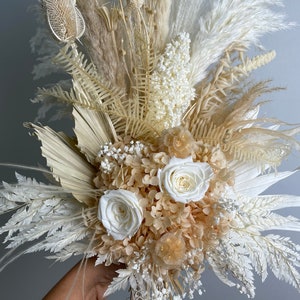 May include: A dried flower bouquet with white and cream dried flowers, including roses, hydrangeas, and pampas grass.