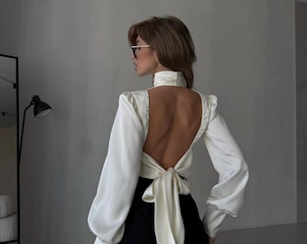 Blusa de satén color marfil con espalda descubierta, mangas largas y cuello alto.