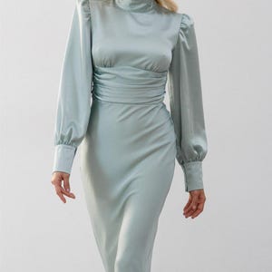Full-length side view of sage green satin midi dress showing the dress length to mid-calf and the smooth sage green satin fabric drape styled with heels