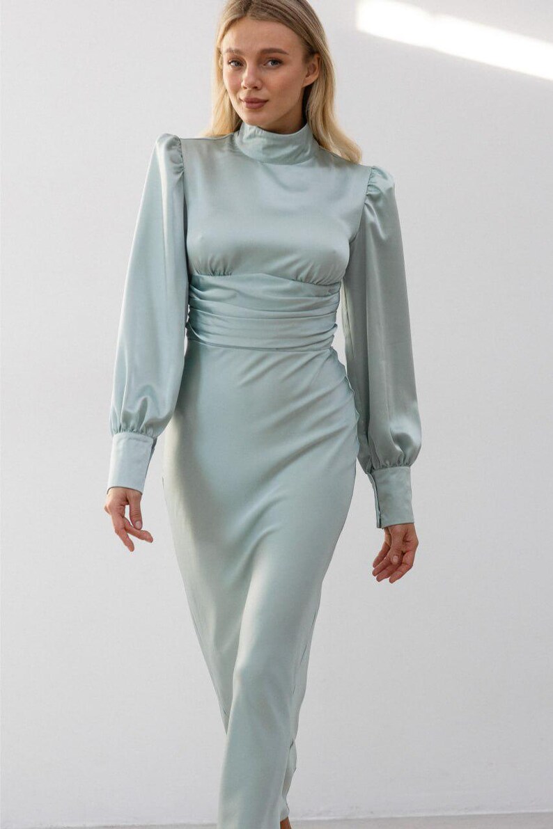 Full-length side view of sage green satin midi dress showing the dress length to mid-calf and the smooth sage green satin fabric drape styled with heels