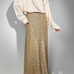 May include: A long, gold sequined skirt with a white satin blouse. The skirt is floor-length and has a fitted waist.