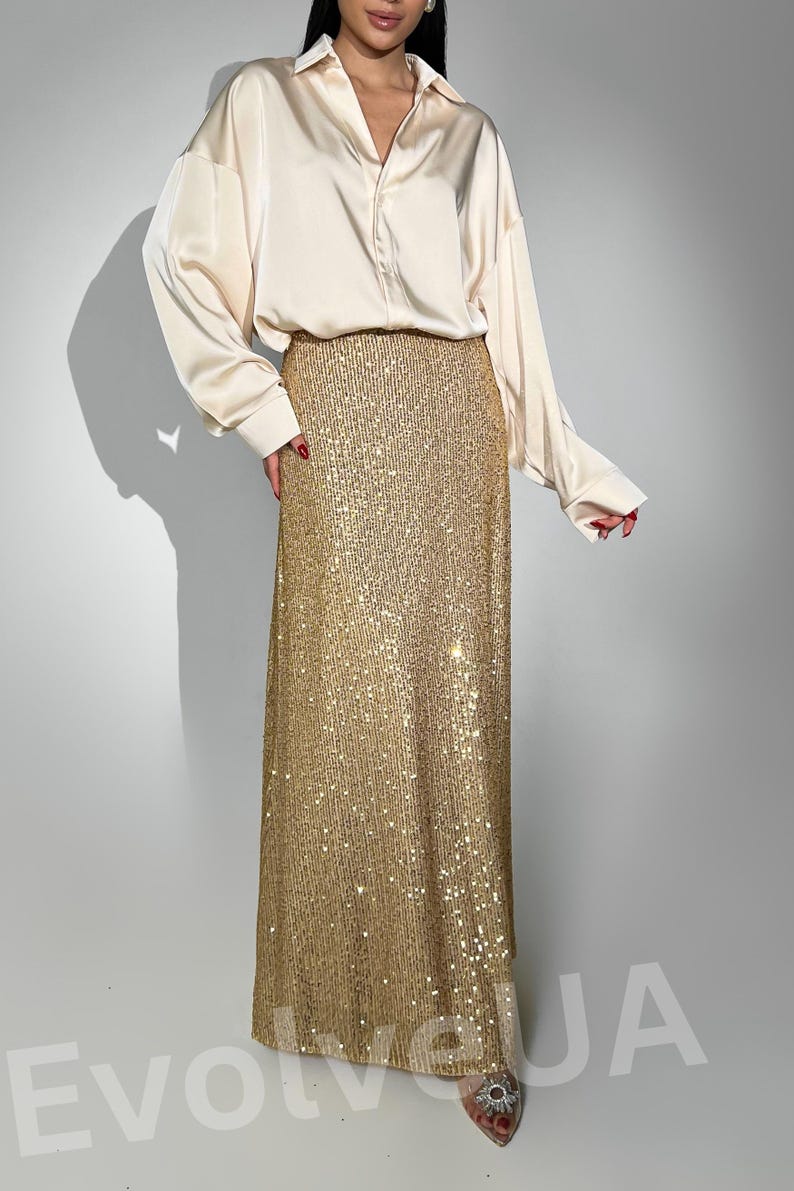 May include: A long, gold sequined skirt with a white satin blouse. The skirt is floor-length and has a fitted waist.