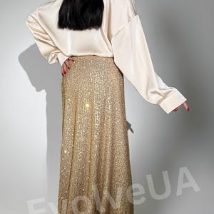 May include: A long gold sequined skirt with a high waist. The skirt is made of small, shimmering sequins and has a flowing, A-line silhouette.