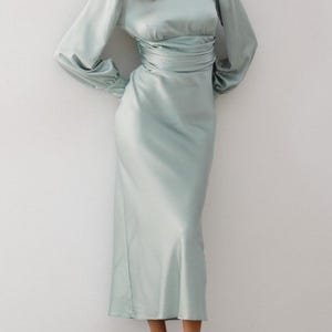 Full-length front view of sage green satin midi dress on model showing the complete silhouette — turtleneck, long sleeves, fitted waist — and the soft muted sage green color