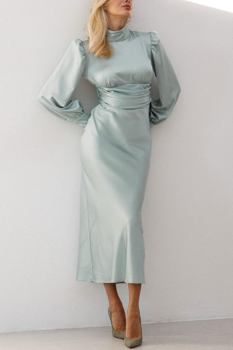 Full-length front view of sage green satin midi dress on model showing the complete silhouette — turtleneck, long sleeves, fitted waist — and the soft muted sage green color