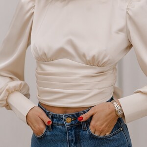 Three-quarter front view of the ivory silk blend turtleneck blouse showing the high neck, bishop sleeves with slight shoulder puff, and fitted cropped bodice; neutral background.