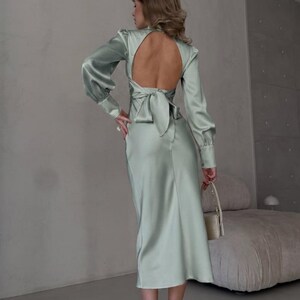 Full-length back view of sage green satin midi dress showing the open back construction and self-tie bow detail at the center back styled with gold heels