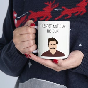 May include: White ceramic mug featuring a cartoon illustration of Ron Swanson from the TV show Parks and Recreation. The mug has black text that reads "I regret nothing. The end."