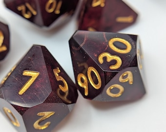 Deep red dungeons and dragons dice with veins of sparkly gold and bright gold inked numbers.