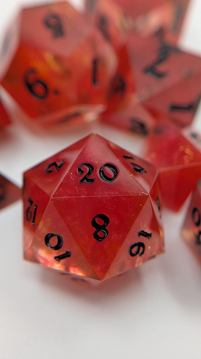 May include: A collection of red polyhedral dice with black numerals. The dice are made from a translucent material, revealing their internal structure. The image features several dice, including a prominent twenty-sided die, perfect for role-playing games.