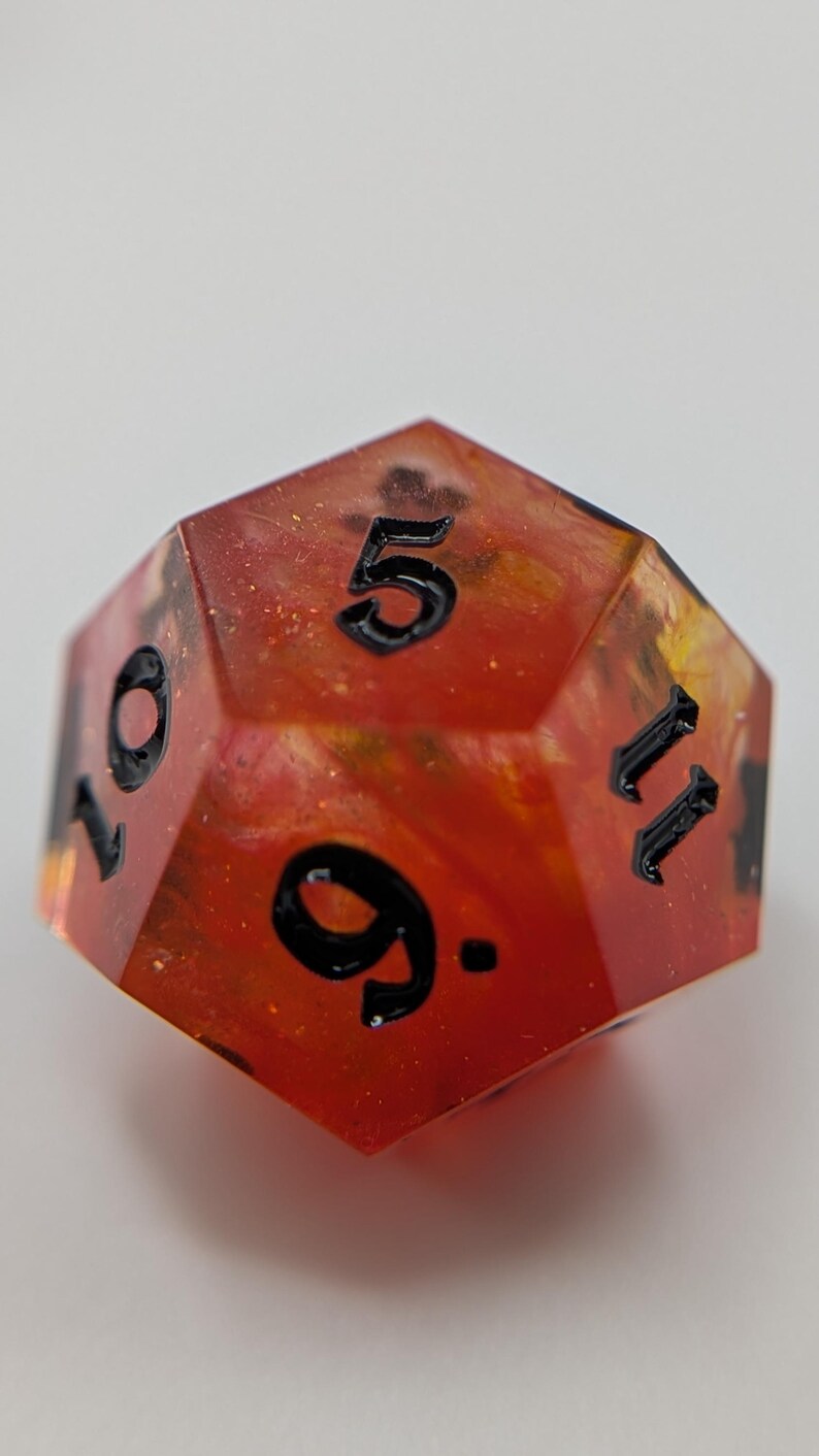 May include: A twelve-sided polyhedral die with a red and orange interior, and black numbers. The die displays the numbers 5, 9, 10, and 11. This unique die is suitable for tabletop gaming.