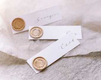 Può includere: Tre carte rettangolari bianche con sigilli di cera dorata. Le carte hanno nomi scritti a mano: "Georgie", "Trey" e "Emily".