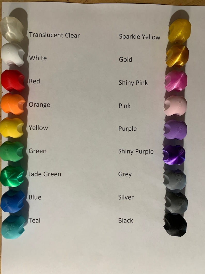 May include: A chart showing 14 different colors of plastic filament for 3D printing. The colors are: Translucent Clear, White, Red, Orange, Yellow, Green, Jade Green, Blue, Teal, Sparkle Yellow, Gold, Shiny Pink, Pink, Purple, Shiny Purple, Grey, Silver, and Black.