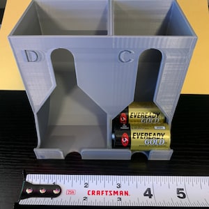May include: A gray plastic battery organizer with two compartments labeled "D" and "C". The organizer is holding two sets of batteries, one set of "C" size batteries and one set of "D" size batteries. The batteries are Eveready Gold brand.