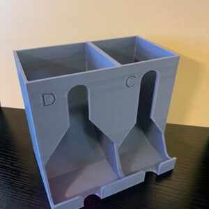 May include: A gray plastic card holder with two compartments labeled "C" and "D". The holder has three slots for cards in each compartment.