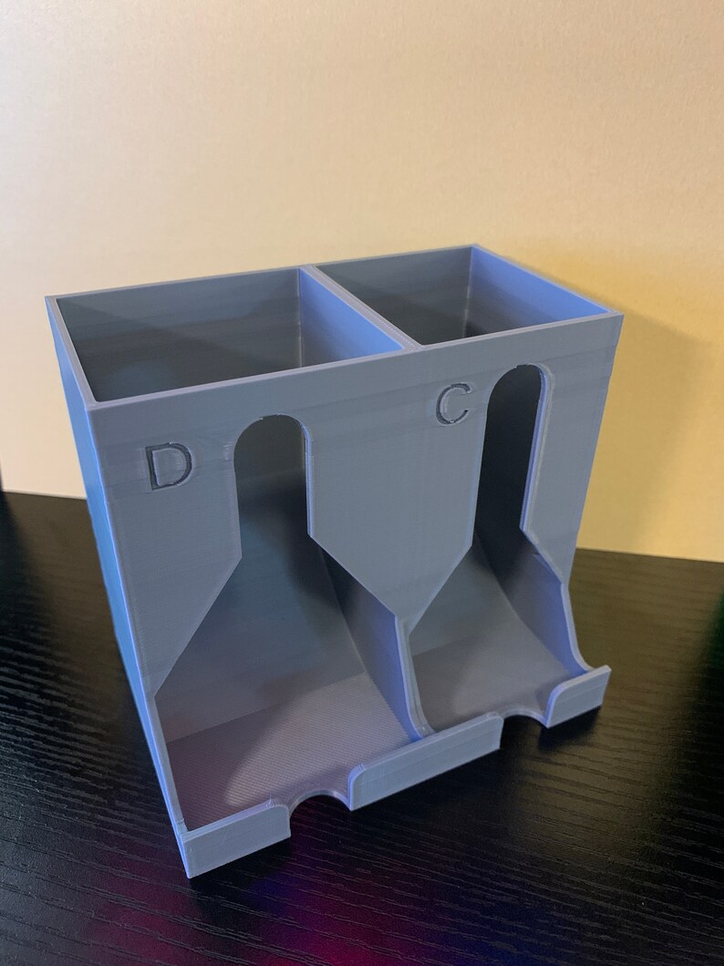 May include: A gray plastic card holder with two compartments labeled "C" and "D". The holder has three slots for cards in each compartment.