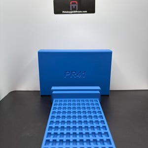 May include: A bright blue rectangular storage organizer featuring a vertical back panel embossed with the text PR41 and a horizontal base with a grid of small square compartments for holding items. A black logo sign is visible in the background.