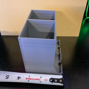 May include: A gray plastic organizer with two compartments and a side shelf. The organizer is 3 inches wide.