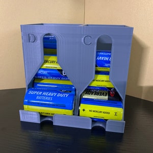 May include: A gray plastic battery organizer with two compartments labeled "D" and "C". The organizer is filled with various brand batteries, including "Eveready" and "Circuit City".