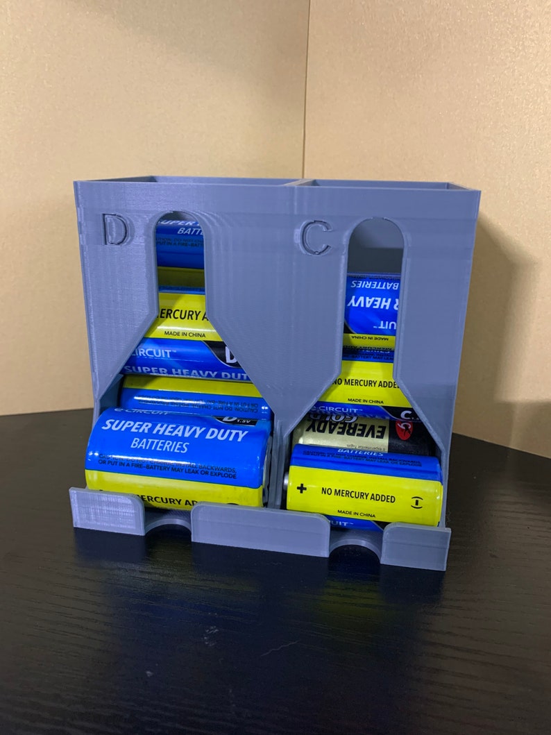 May include: A gray plastic battery organizer with two compartments labeled "D" and "C". The organizer is filled with various brand batteries, including "Eveready" and "Circuit City".