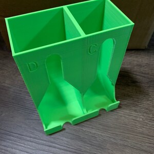 May include: A green plastic organizer with two compartments, labeled "C" and "D", for storing small items.