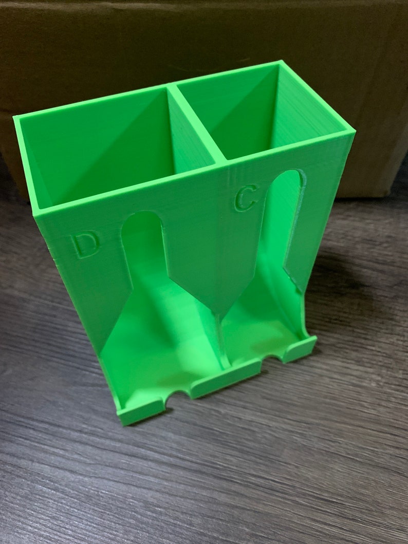 May include: A green plastic organizer with two compartments, labeled "C" and "D", for storing small items.