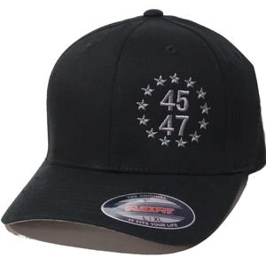 May include: Black Flexfit baseball cap with a curved peak. The cap displays the numbers "45" and "47" in white, encircled by white stars. The Flexfit logo is visible on the peak.