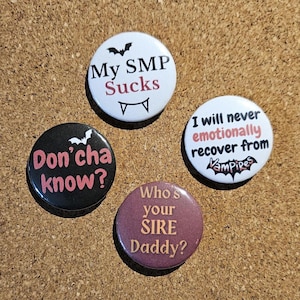 May include: Four circular badges with vampire-themed text and graphics. One badge reads "My SMP Sucks" with a bat and fangs. Another says "Don'cha know?" with a bat. A third says "I will never emotionally recover from Vampires". The last says "Who's your SIRE Daddy?"