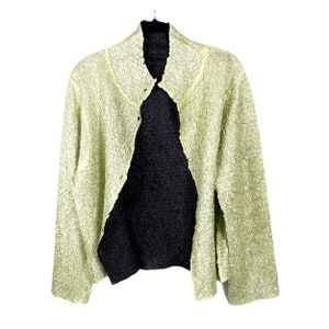 以下が含まれることがあります： 黒ボタン留めの薄い緑色のテクスチャードカーディガン。カーディガンはハイネックで長袖です。