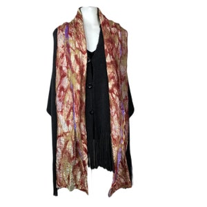 May include: A long, rectangular scarf with a brown, gold, and purple abstract pattern. The scarf is draped over a black cardigan with fringe.