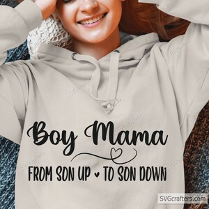 May include: A light grey hoodie with the text "Boy Mama" in black cursive font. The text "FROM SON UP TO SON DOWN" is also in black font with a small heart symbol between the two phrases.