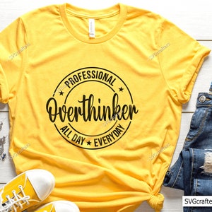Op de afbeelding: Geel T-shirt met een zwarte cirkelvormige afbeelding met de tekst "Professional Overthinker All Day Everyday".