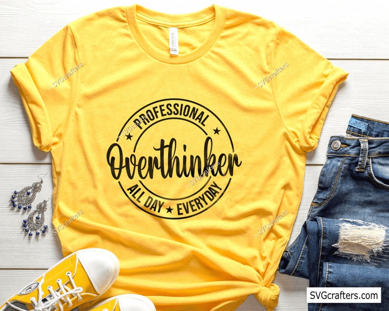 Op de afbeelding: Geel T-shirt met een zwarte cirkelvormige afbeelding met de tekst "Professional Overthinker All Day Everyday".