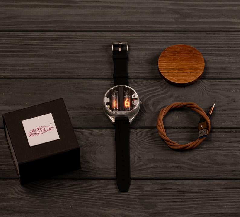 May include: A silver-cased watch with a black band displays the number 6 in orange. The watch is next to a brown wooden coaster, a brown USB cable, and a black box with a white label that reads "NEON GEAR".
